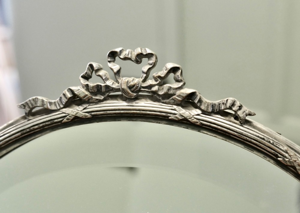 An arched French Art Deco silver-plated vanity mirror featuring bevelled glass and a decorative ribbon cresting. View V