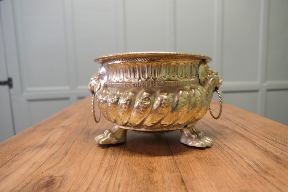 An ornate round brass jardiniere featuring gadrooned ribbed sides, lion mask ring handles, and paw feet. View II
