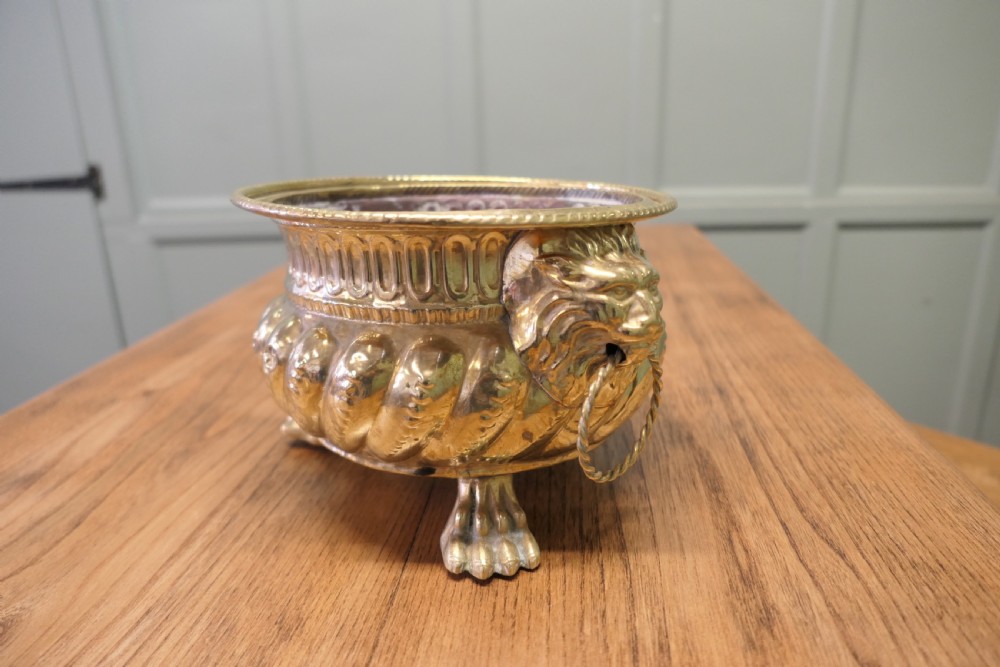 An ornate round brass jardiniere featuring gadrooned ribbed sides, lion mask ring handles, and paw feet. View III