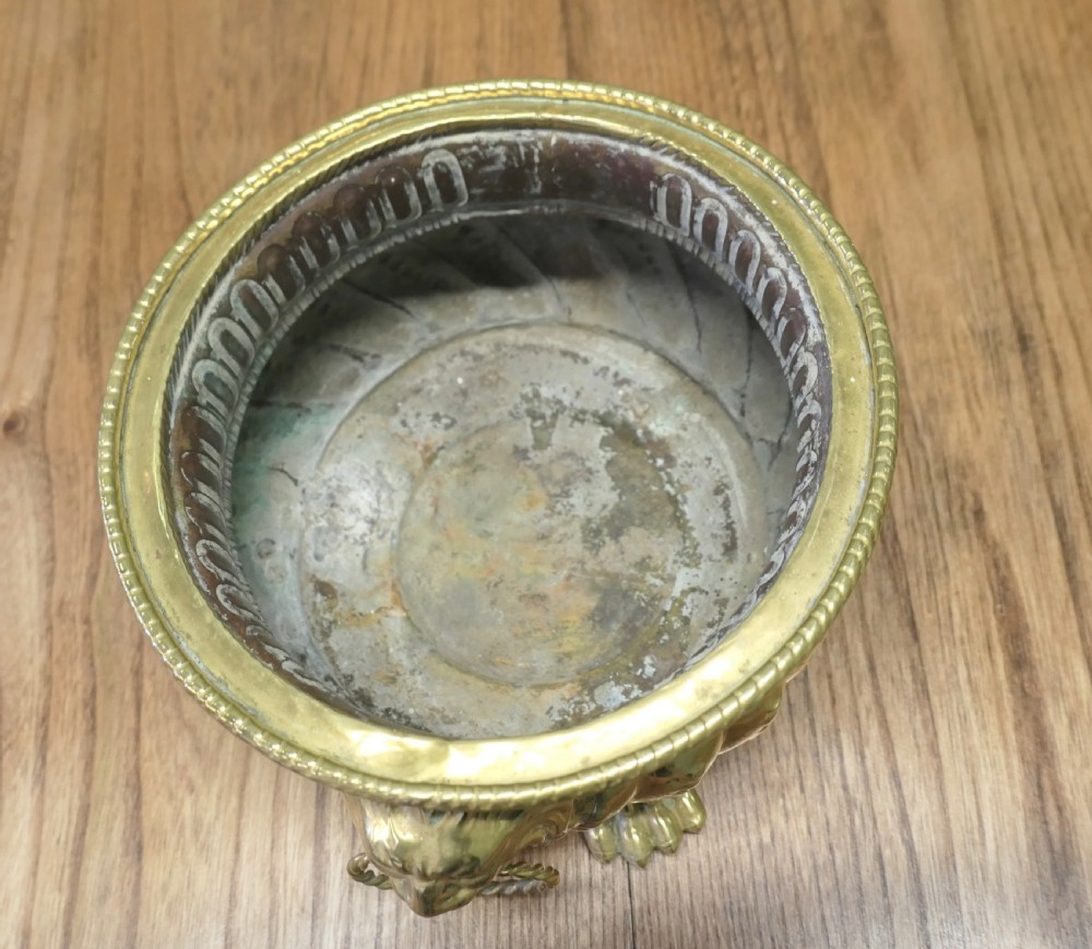 An ornate round brass jardiniere featuring gadrooned ribbed sides, lion mask ring handles, and paw feet. View IV