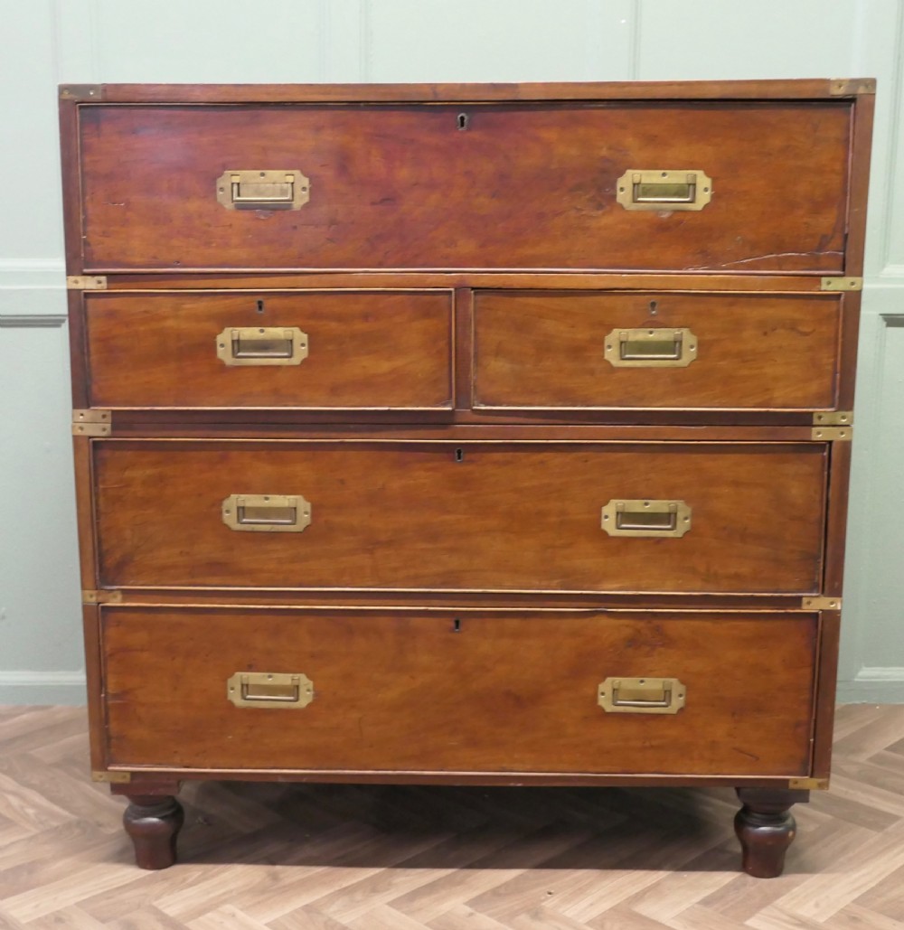 A two-section antique teak military campaign chest featuring brass corner straps, flush brass handles, turned feet, and a top secretaire drawer.