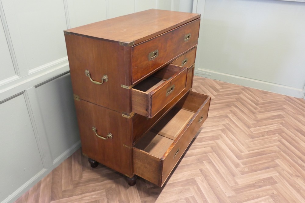A two-section antique teak military campaign chest featuring brass corner straps, flush brass handles, turned feet, and a top secretaire drawer. View II