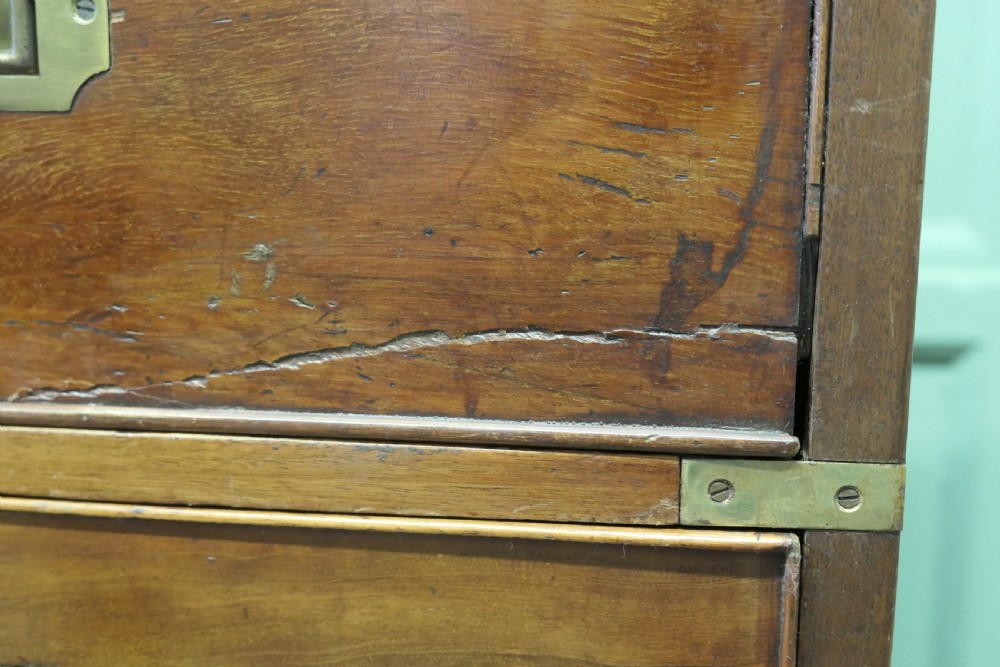 A two-section antique teak military campaign chest featuring brass corner straps, flush brass handles, turned feet, and a top secretaire drawer. View III