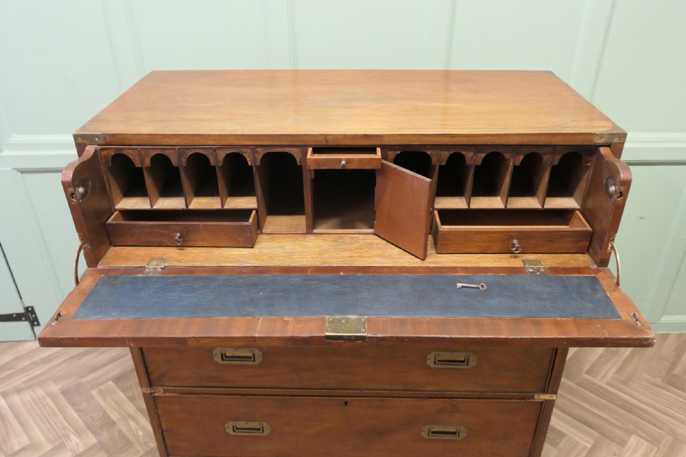 A two-section antique teak military campaign chest featuring brass corner straps, flush brass handles, turned feet, and a top secretaire drawer. View V