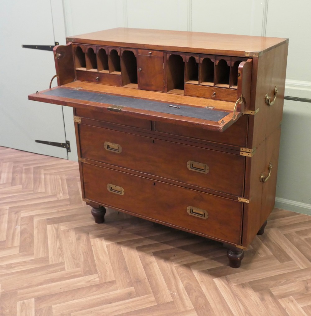 A two-section antique teak military campaign chest featuring brass corner straps, flush brass handles, turned feet, and a top secretaire drawer. View VI