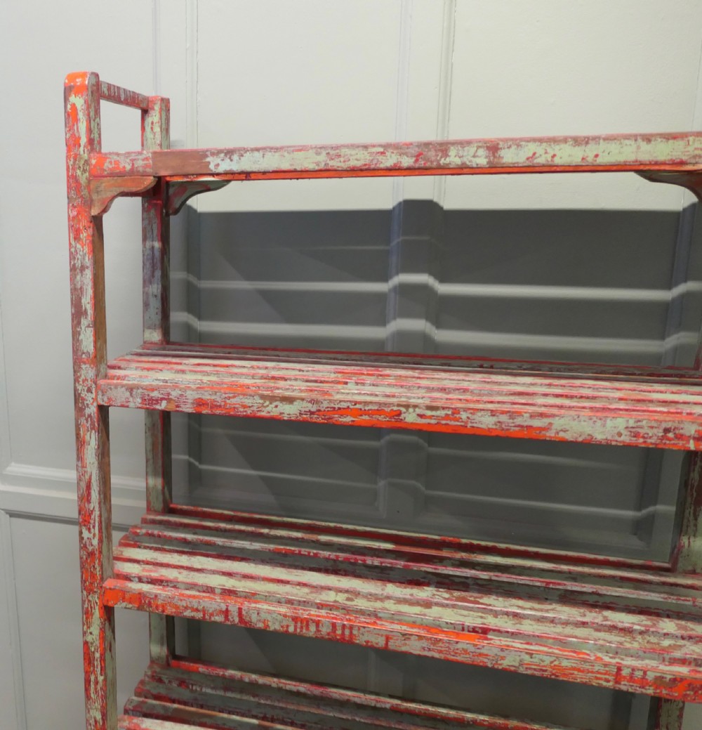 A tall freestanding French wooden shelving unit featuring five slatted shelves and a heavily distressed terracotta red and sage green painted finish. View V