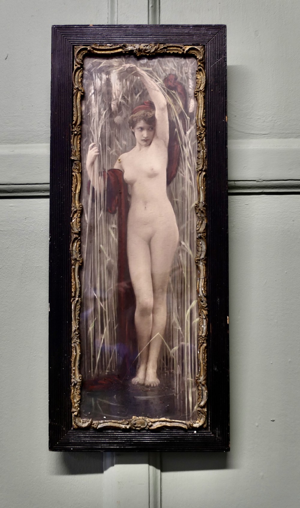 A vertical framed print depicting a classical female figure standing among tall reeds, encased within an ornate gilt inner moulding and a ribbed black timber frame.