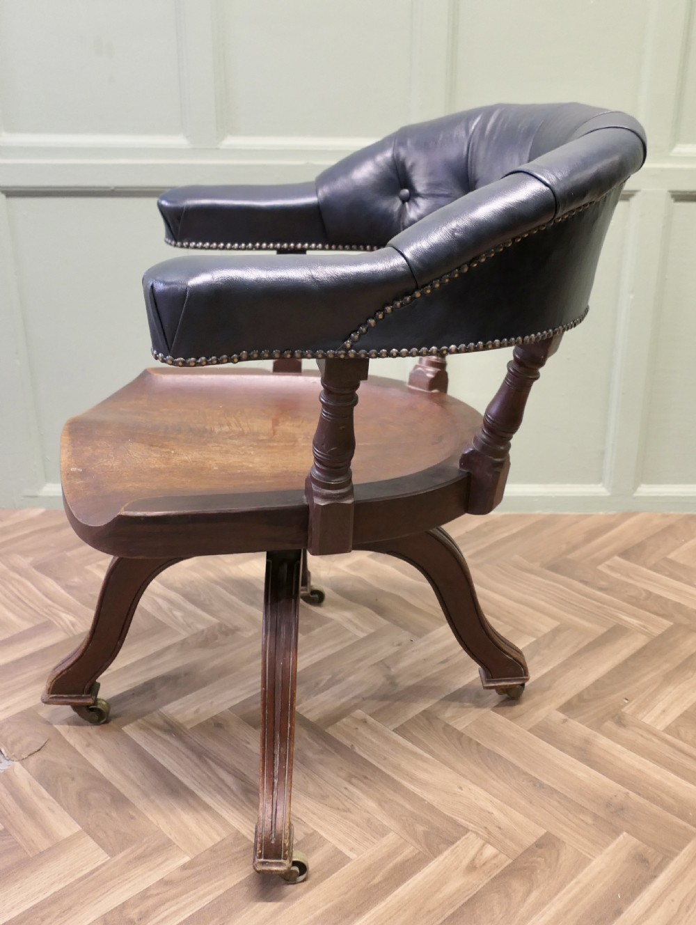 A Victorian mahogany swivel desk chair featuring a buttoned dark leather curved backrest, turned spindles, a shaped timber seat, and four splayed legs with brass castors. View III