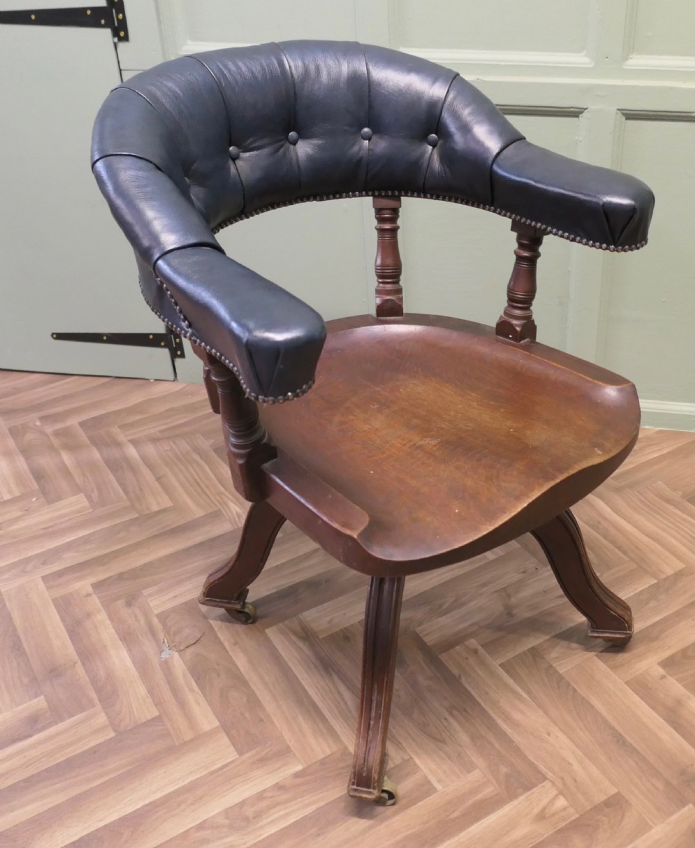 A Victorian mahogany swivel desk chair featuring a buttoned dark leather curved backrest, turned spindles, a shaped timber seat, and four splayed legs with brass castors. View VI