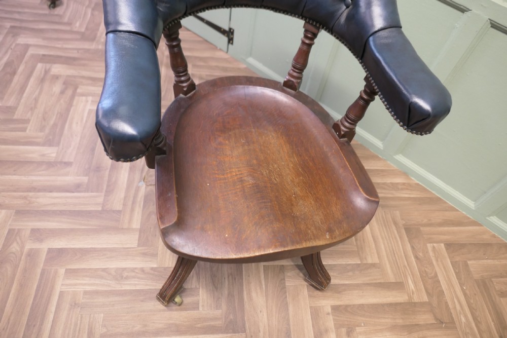 A Victorian mahogany swivel desk chair featuring a buttoned dark leather curved backrest, turned spindles, a shaped timber seat, and four splayed legs with brass castors. View VII