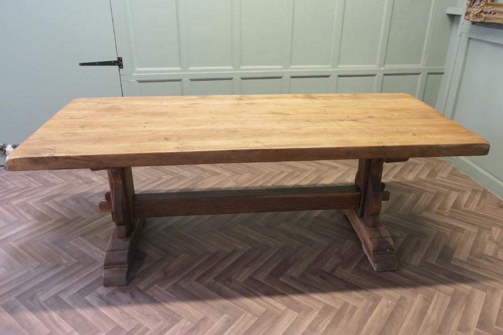 A large French oak monastery dining table featuring a thick rectangular plank top supported by heavy trestle end legs and a pegged stretcher.