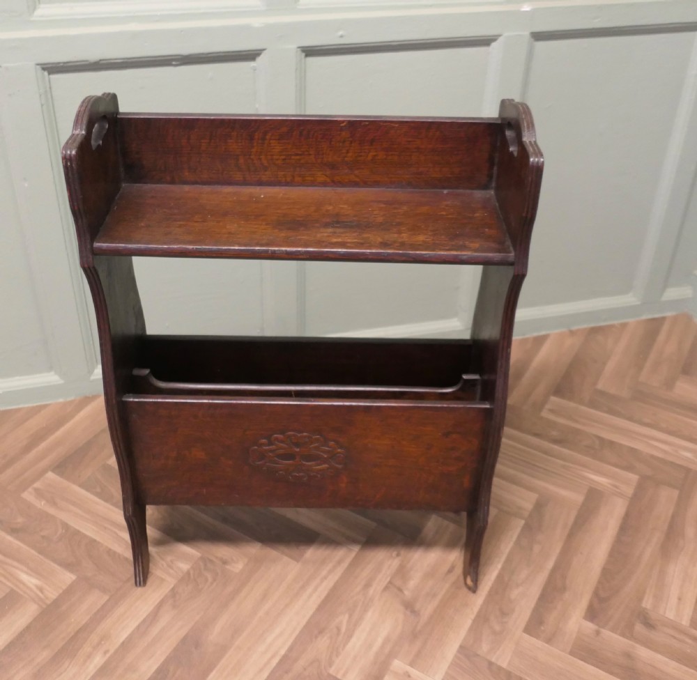 A dark oak Arts and Crafts freestanding bookcase featuring a top shelf, integrated magazine rack with carved motif, and cut-out side handles. View II
