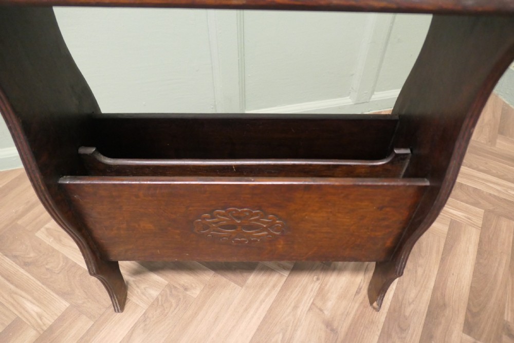 A dark oak Arts and Crafts freestanding bookcase featuring a top shelf, integrated magazine rack with carved motif, and cut-out side handles. View III