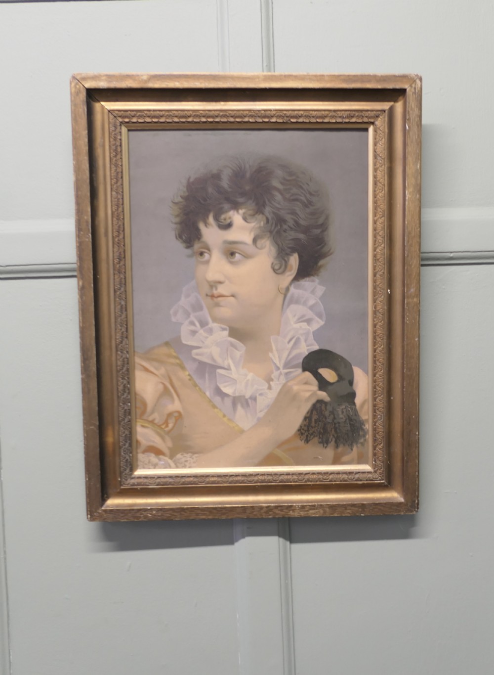 A framed oil portrait painting on board depicting a woman with short curly hair holding a black masquerade mask, dressed in a ruffled collar inside a gilded wood frame.
