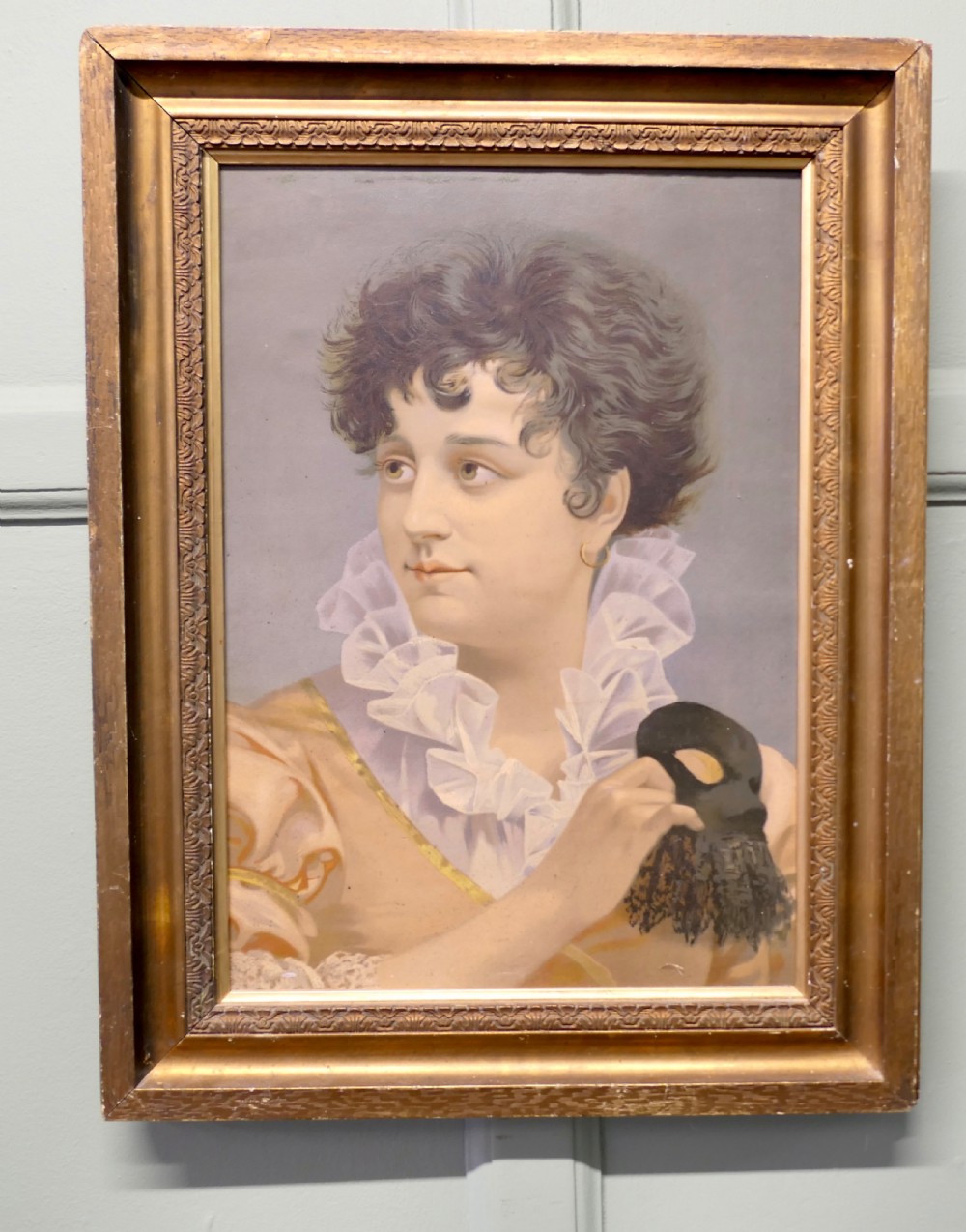 A framed oil portrait painting on board depicting a woman with short curly hair holding a black masquerade mask, dressed in a ruffled collar inside a gilded wood frame. View II