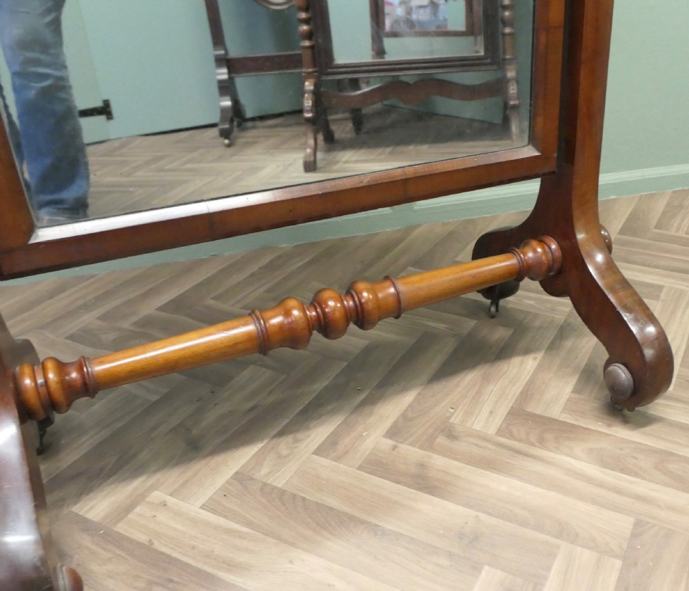 A Victorian mahogany freestanding cheval mirror featuring an arched glass plate suspended between two uprights with a turned cross stretcher and splayed legs with castors. View VI