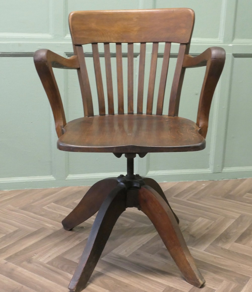 A wooden Art Deco swivel desk chair featuring curved armrests, a slatted backrest, and a splayed four-legged base.