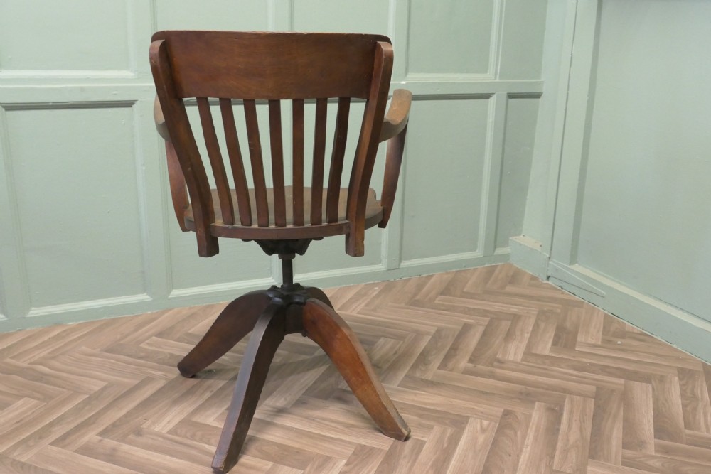 A wooden Art Deco swivel desk chair featuring curved armrests, a slatted backrest, and a splayed four-legged base. View II