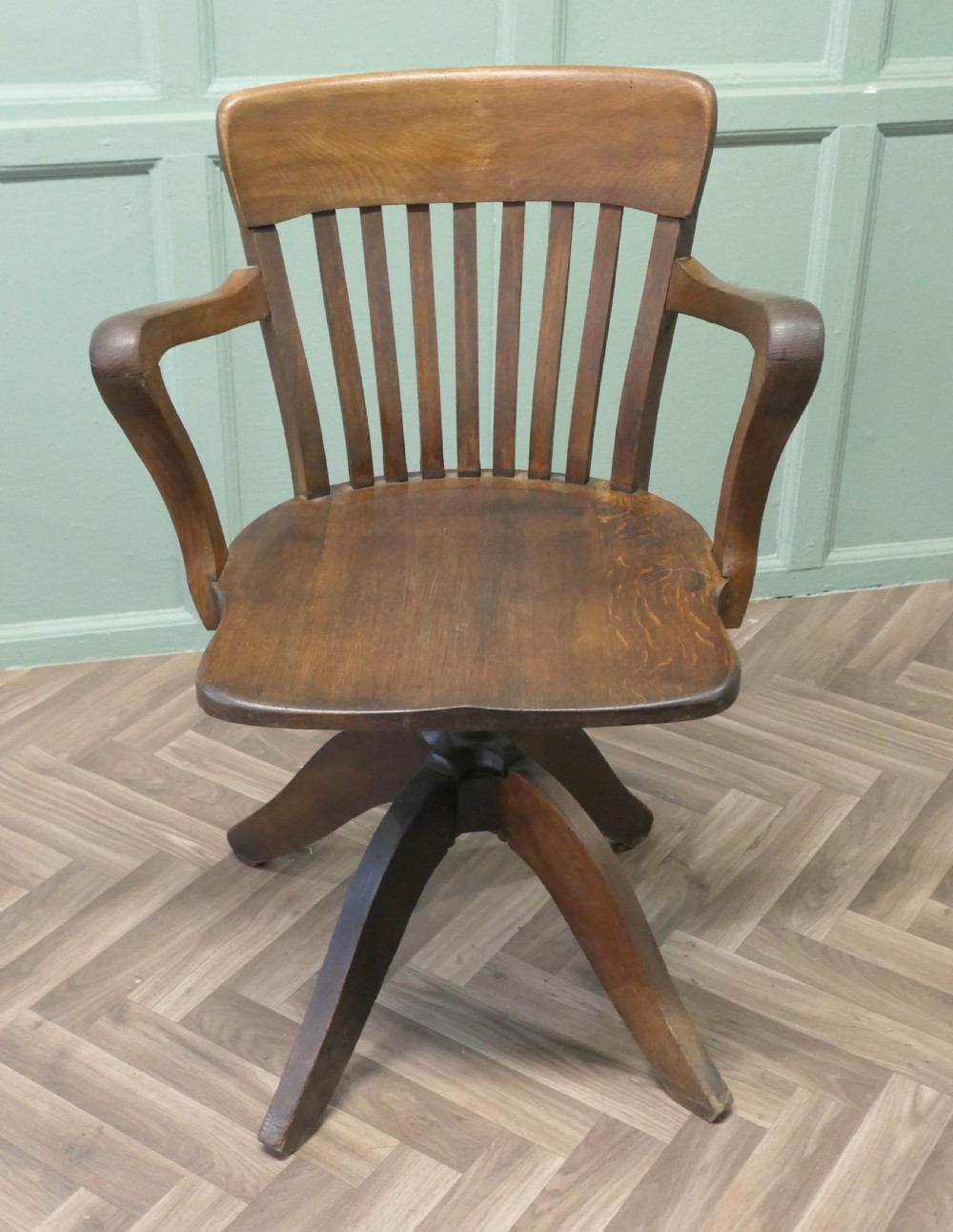 A wooden Art Deco swivel desk chair featuring curved armrests, a slatted backrest, and a splayed four-legged base. View III