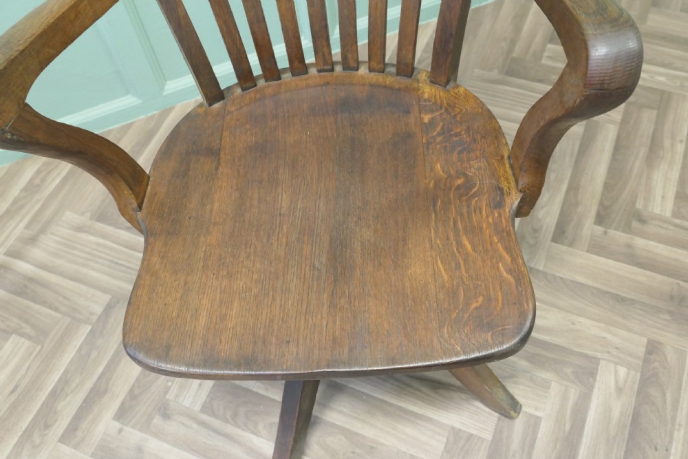 A wooden Art Deco swivel desk chair featuring curved armrests, a slatted backrest, and a splayed four-legged base. View V