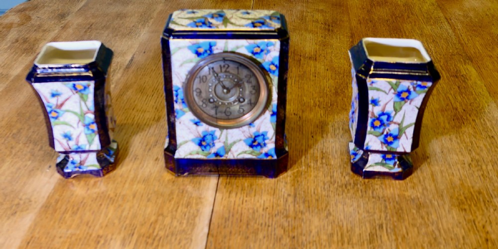 A three-piece French porcelain clock garniture set featuring a central rectangular mantel clock flanked by two matching side vases decorated with blue floral patterns and cobalt blue gilded borders.