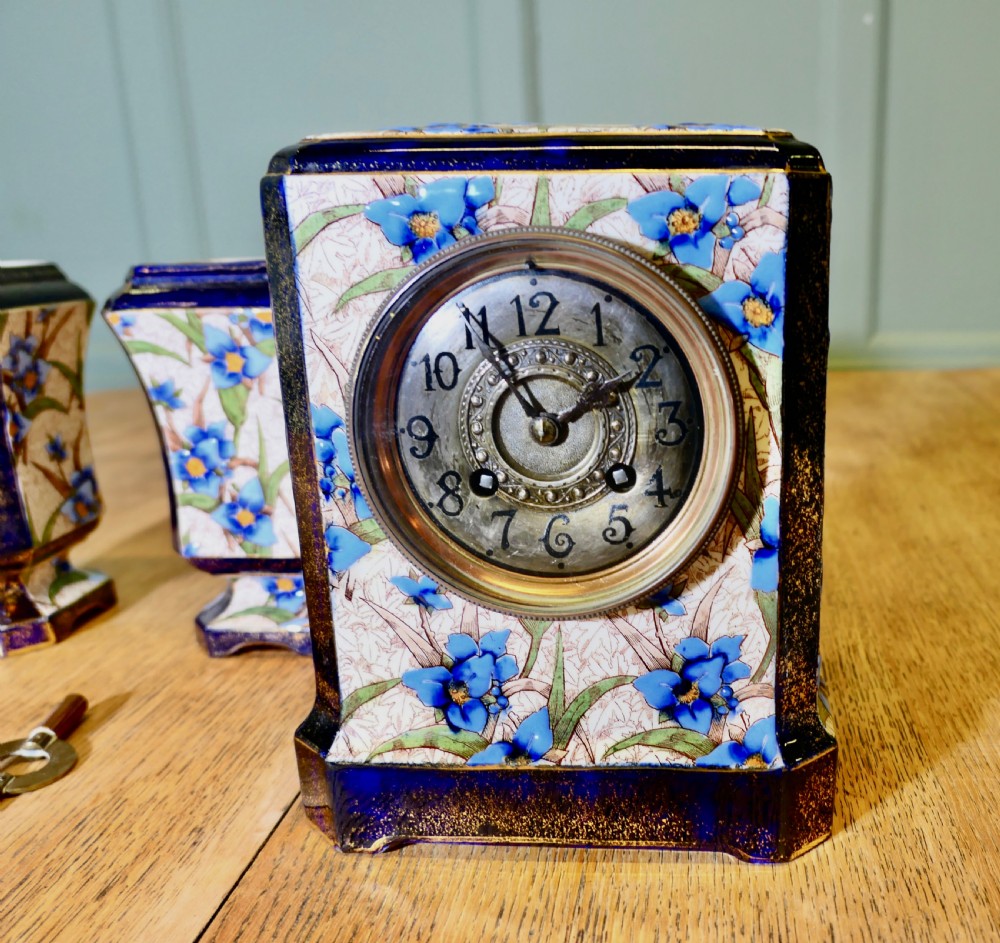 A three-piece French porcelain clock garniture set featuring a central rectangular mantel clock flanked by two matching side vases decorated with blue floral patterns and cobalt blue gilded borders. View II