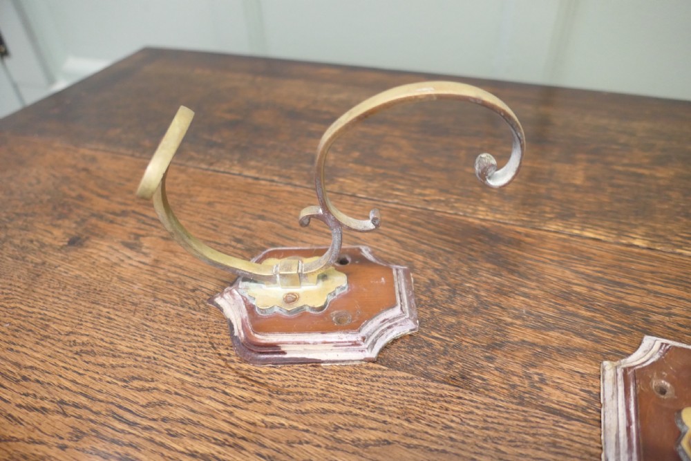 A set of three French artisan brass coat hooks featuring curved double arms mounted onto shield-shaped backplates. View III