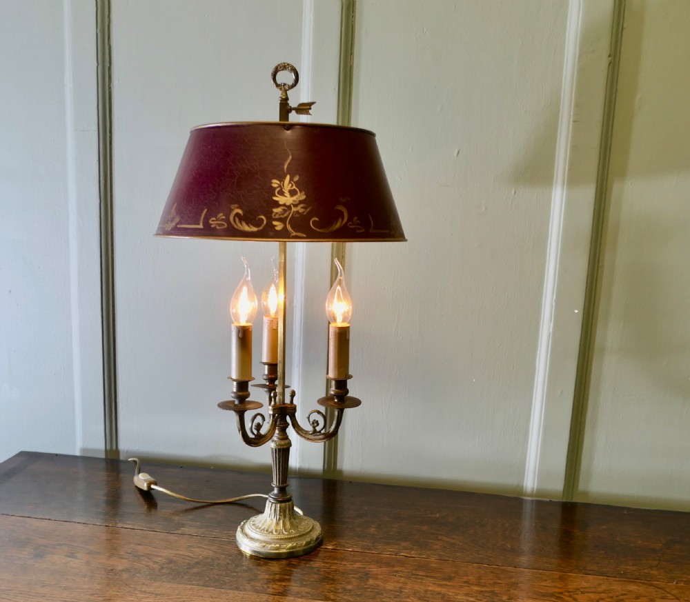 A French toleware and brass desk lamp featuring a burgundy lacquered shade with gilt floral painting and three candle-style light sockets.
