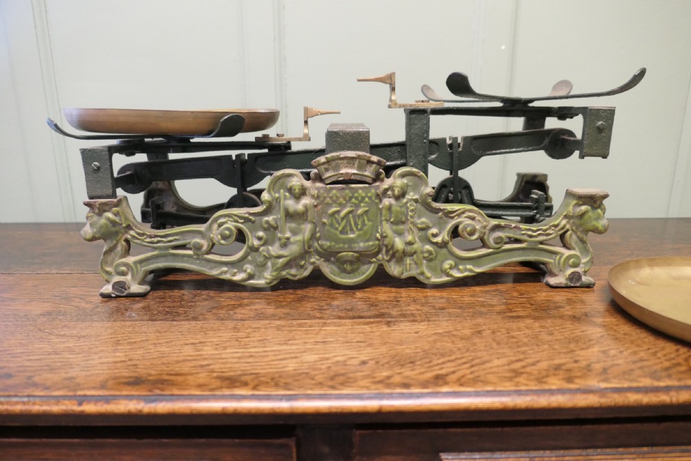 A nineteenth-century French grocers balance scale featuring a green patinated cast iron frame with ornate heraldic relief and double brass pans.