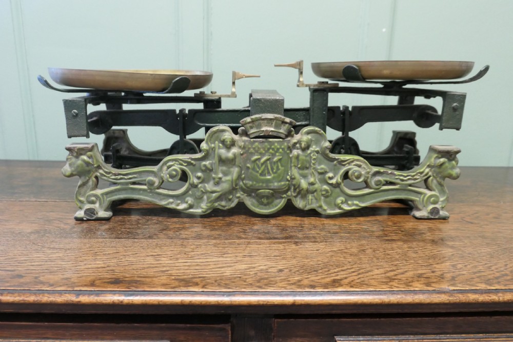 A nineteenth-century French grocers balance scale featuring a green patinated cast iron frame with ornate heraldic relief and double brass pans. View II