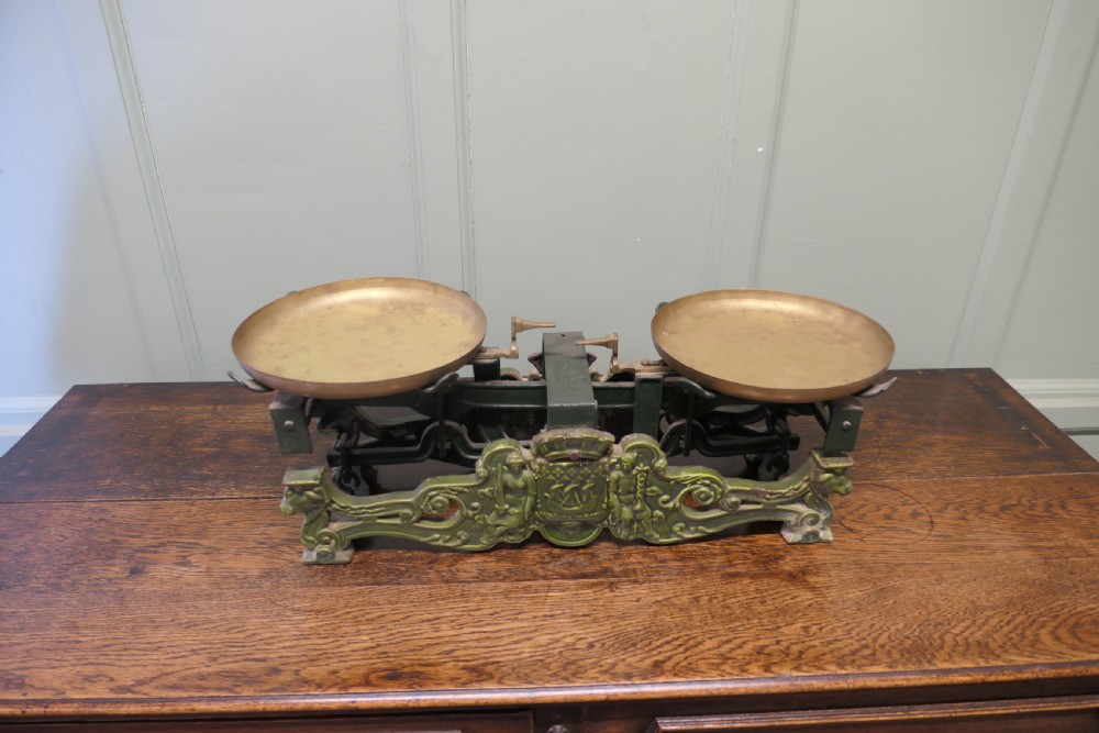 A nineteenth-century French grocers balance scale featuring a green patinated cast iron frame with ornate heraldic relief and double brass pans. View IV