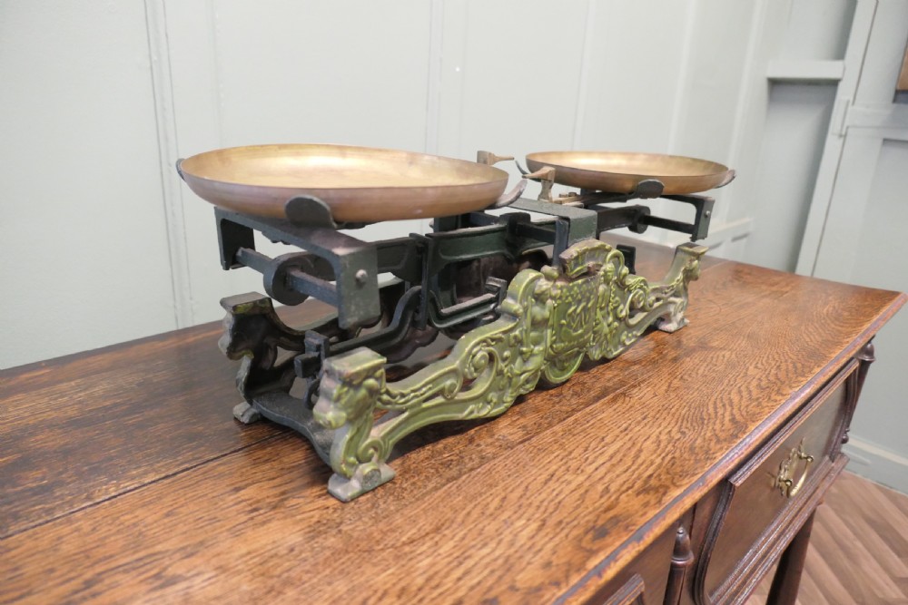 A nineteenth-century French grocers balance scale featuring a green patinated cast iron frame with ornate heraldic relief and double brass pans. View V