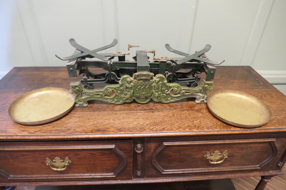 A nineteenth-century French grocers balance scale featuring a green patinated cast iron frame with ornate heraldic relief and double brass pans. View VI