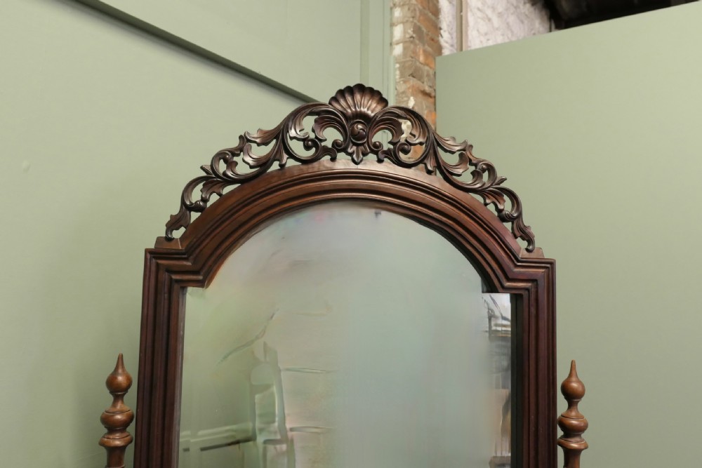A Victorian carved mahogany cheval dressing mirror with an arched cresting top frame and turned side columns on splayed legs. View II