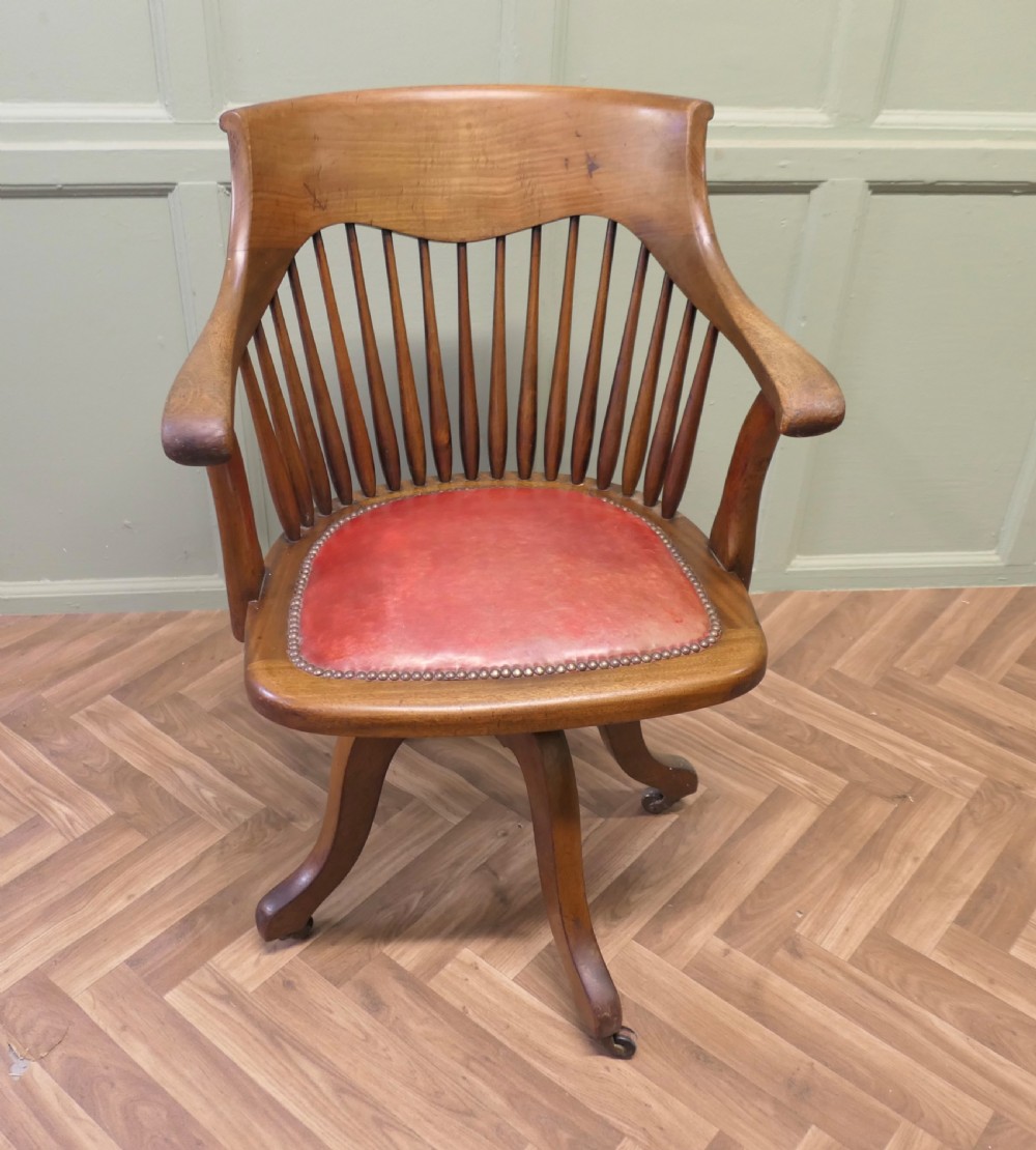 An Arts and Crafts wooden swivel desk chair with a spindle back, curved armrests, a studded leather seat, and a quadruped base with castors. View III