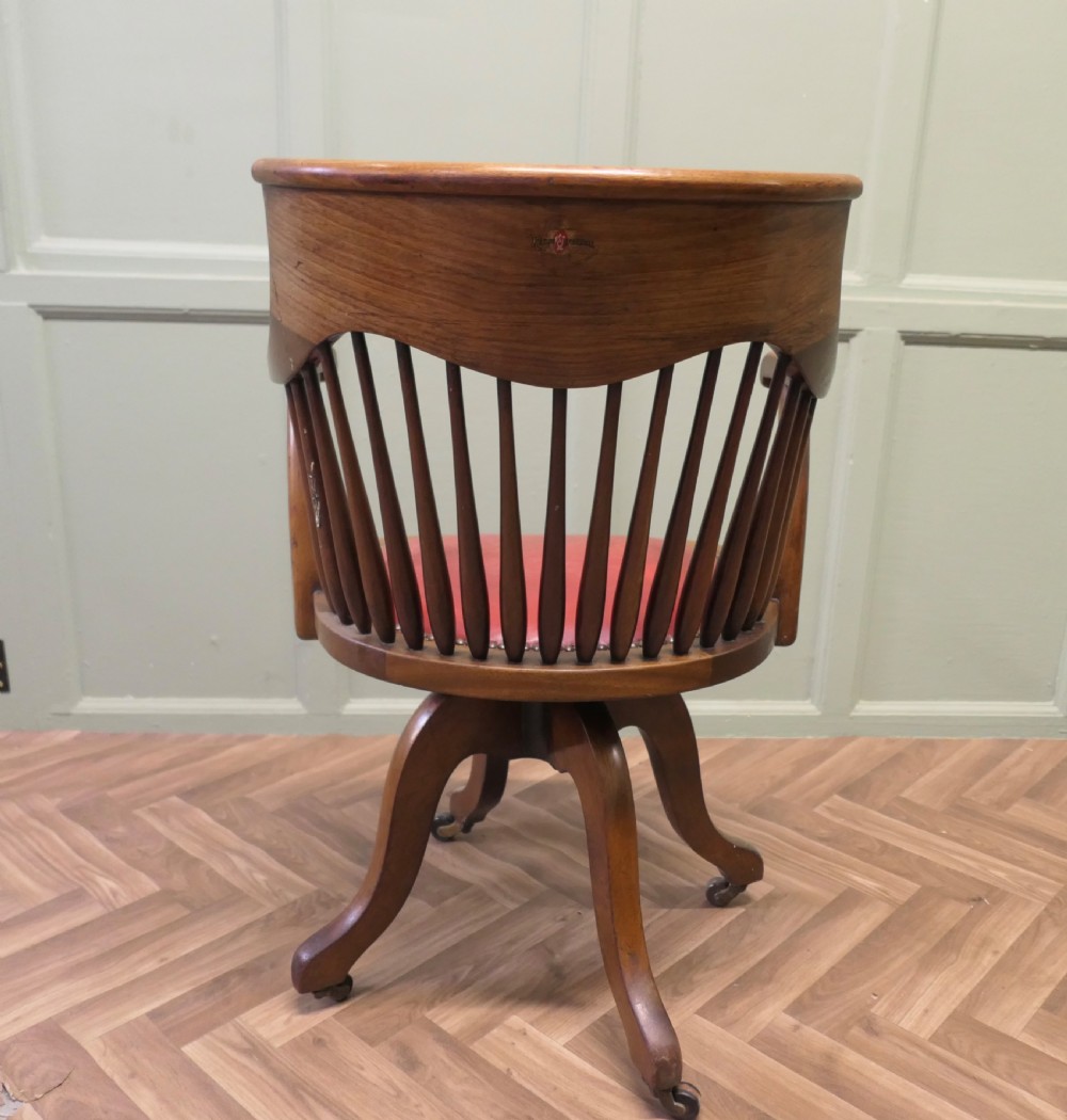 An Arts and Crafts wooden swivel desk chair with a spindle back, curved armrests, a studded leather seat, and a quadruped base with castors. View V