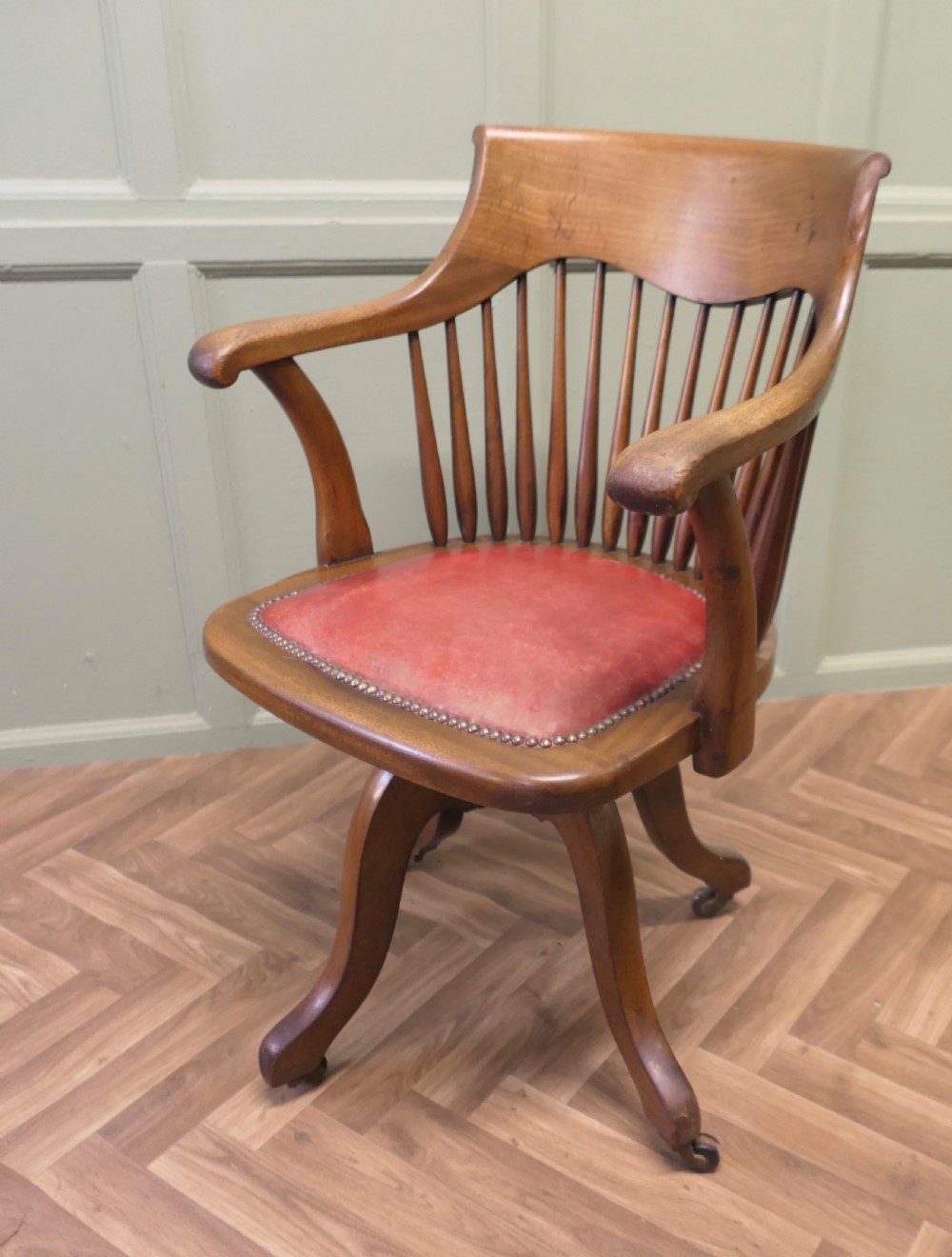 An Arts and Crafts wooden swivel desk chair with a spindle back, curved armrests, a studded leather seat, and a quadruped base with castors. View VI