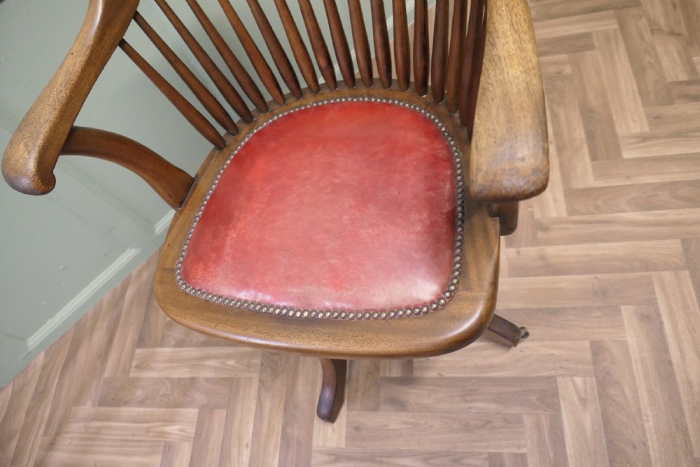 An Arts and Crafts wooden swivel desk chair with a spindle back, curved armrests, a studded leather seat, and a quadruped base with castors. View VII