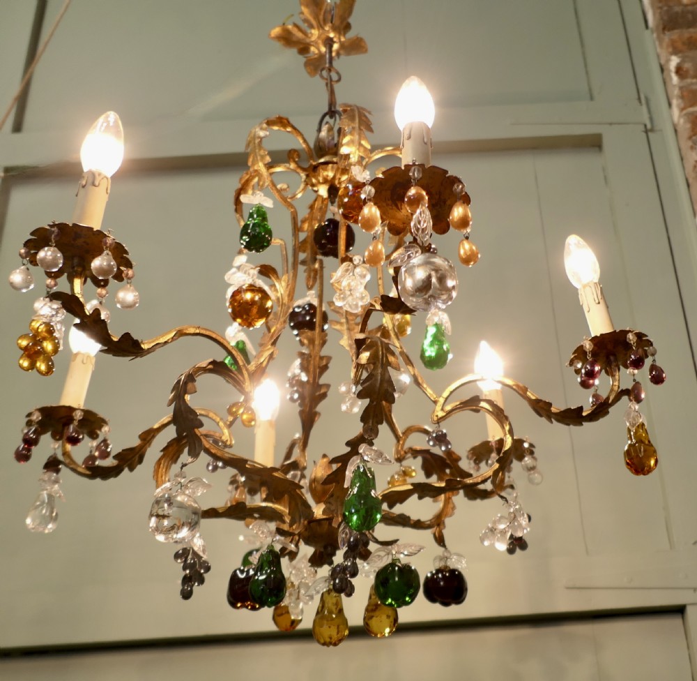 A six-arm gilt-metal chandelier decorated with scrolled leaf motifs and suspended with multicoloured glass fruit drops. View V