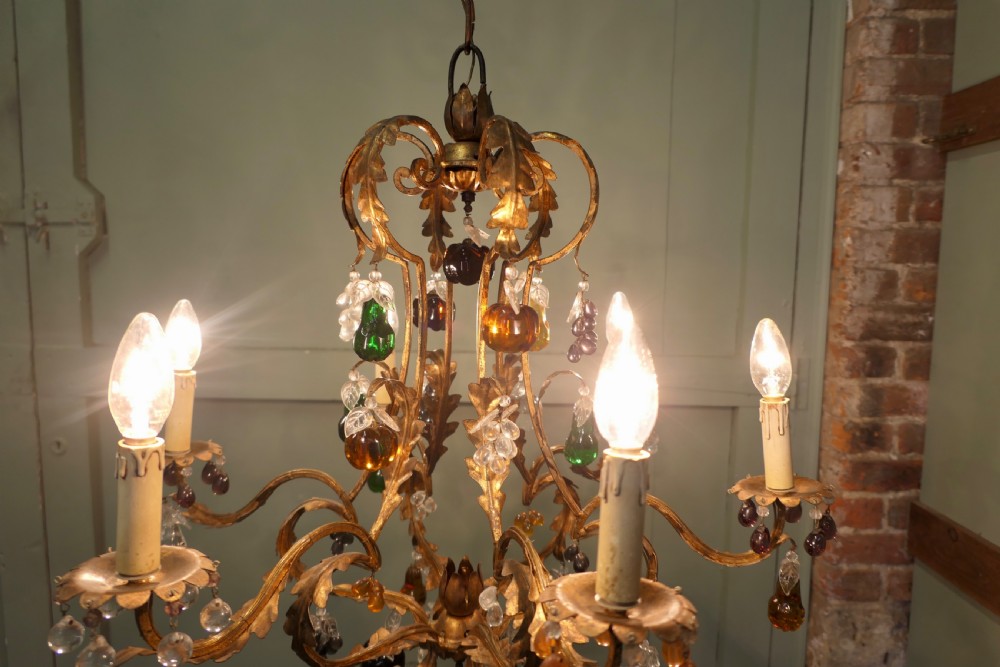 A six-arm gilt-metal chandelier decorated with scrolled leaf motifs and suspended with multicoloured glass fruit drops. View VI