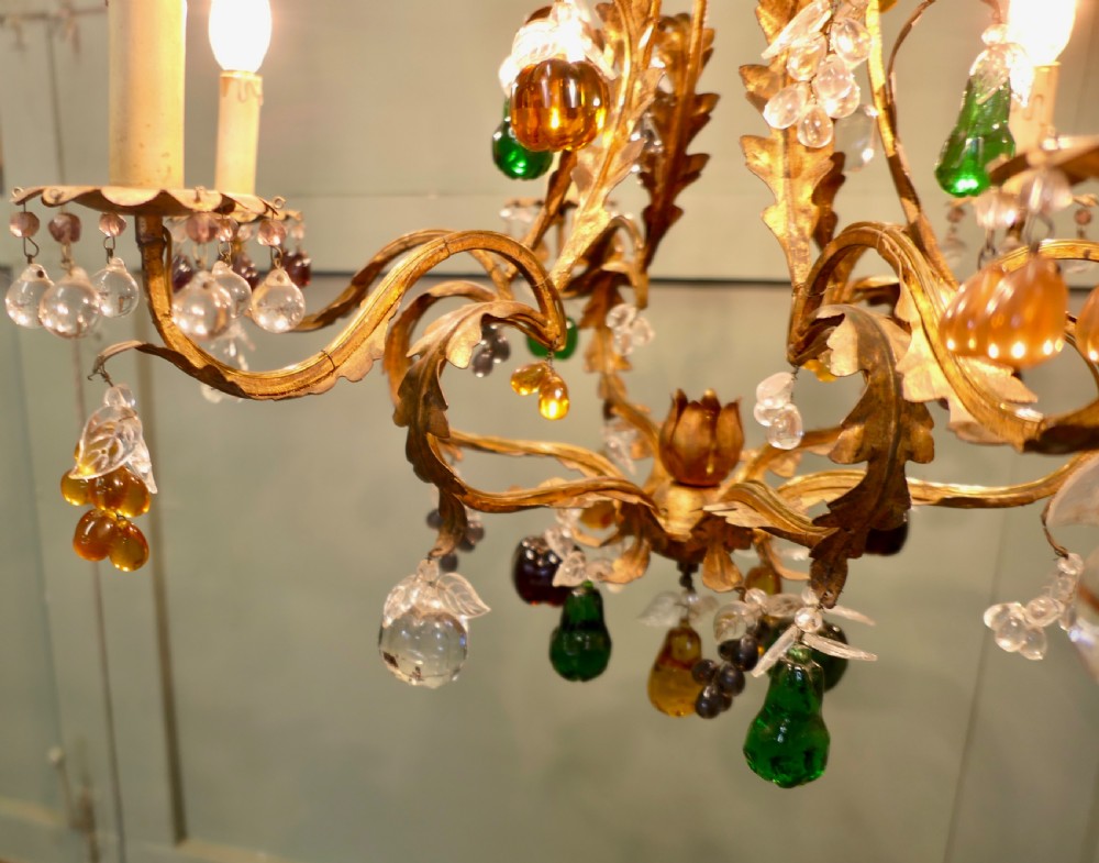 A six-arm gilt-metal chandelier decorated with scrolled leaf motifs and suspended with multicoloured glass fruit drops. View VII