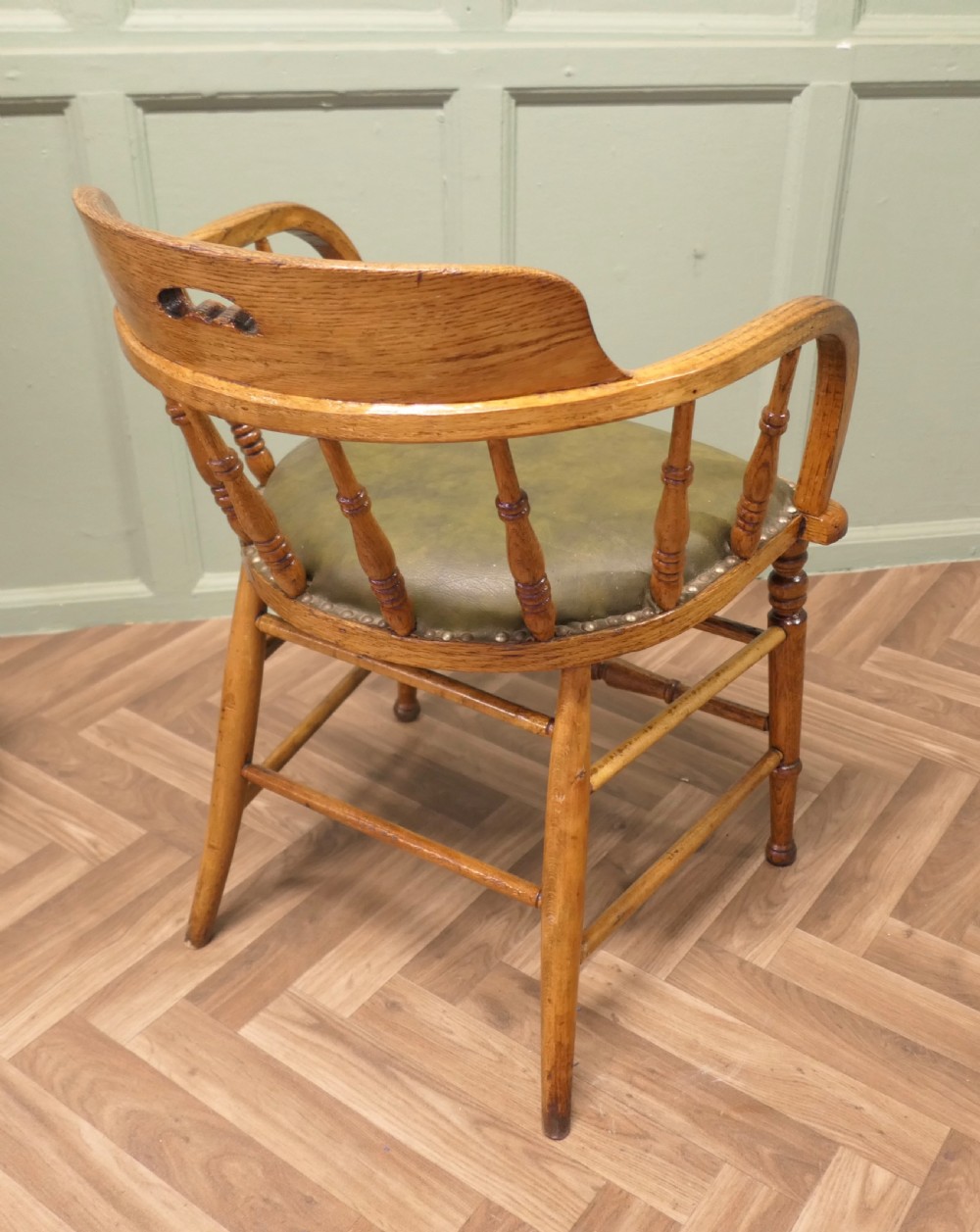 A golden oak smokers bow armchair featuring turned spindles, a steam-bent curved top rail, double stretchers, and a padded green leather seat secured with studs. View V