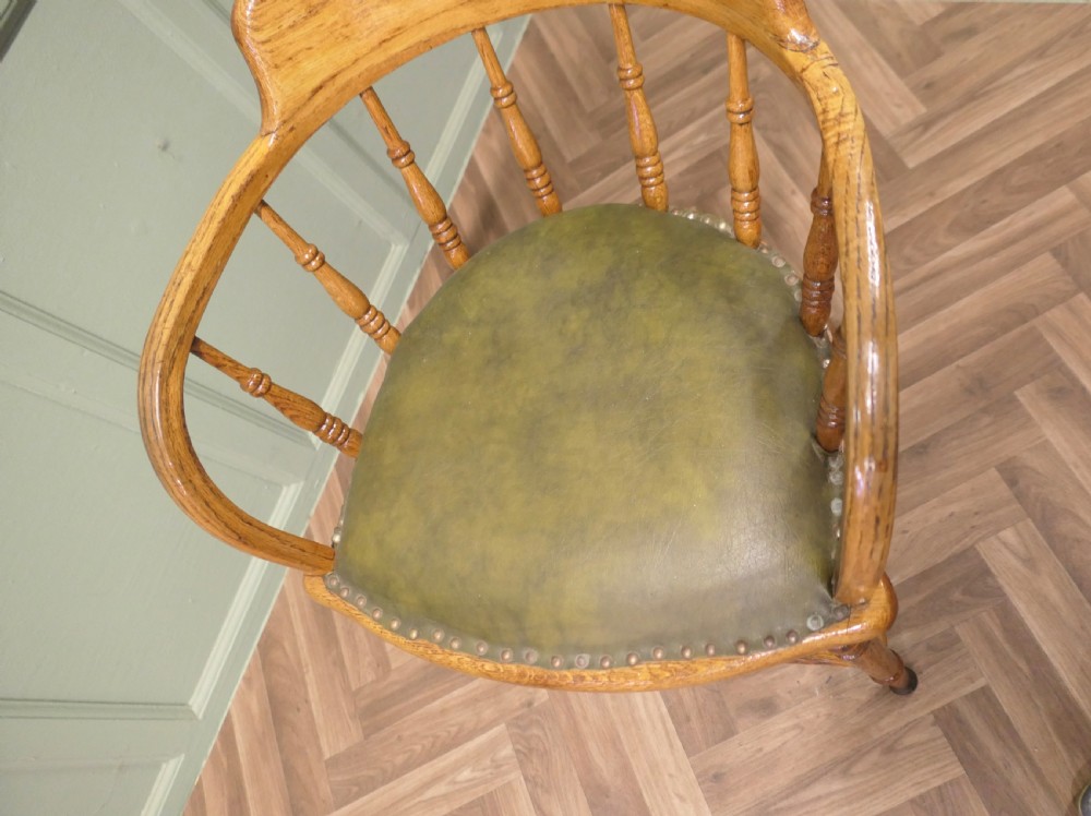 A golden oak smokers bow armchair featuring turned spindles, a steam-bent curved top rail, double stretchers, and a padded green leather seat secured with studs. View VII