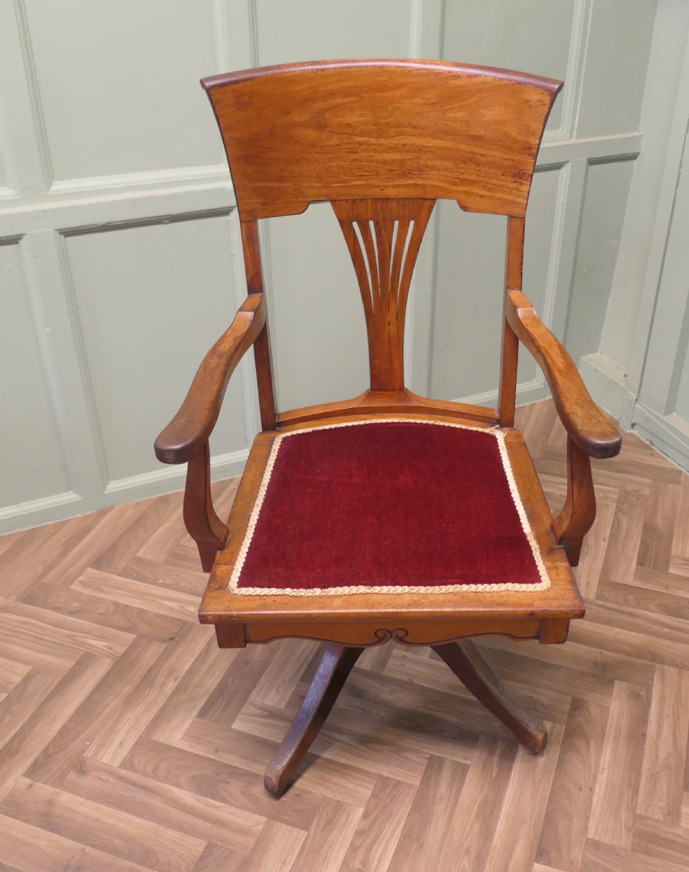 An Edwardian Arts and Crafts walnut revolving desk chair with a curved backrest, carved splat detail, shaped armrests, and a red velvet seat insert. View II