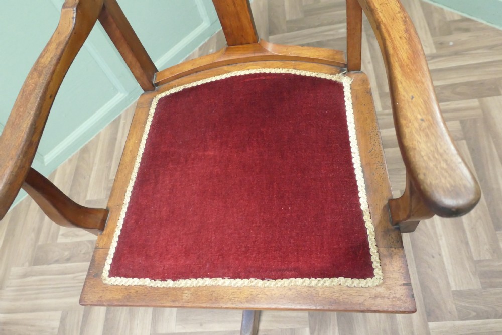 An Edwardian Arts and Crafts walnut revolving desk chair with a curved backrest, carved splat detail, shaped armrests, and a red velvet seat insert. View III