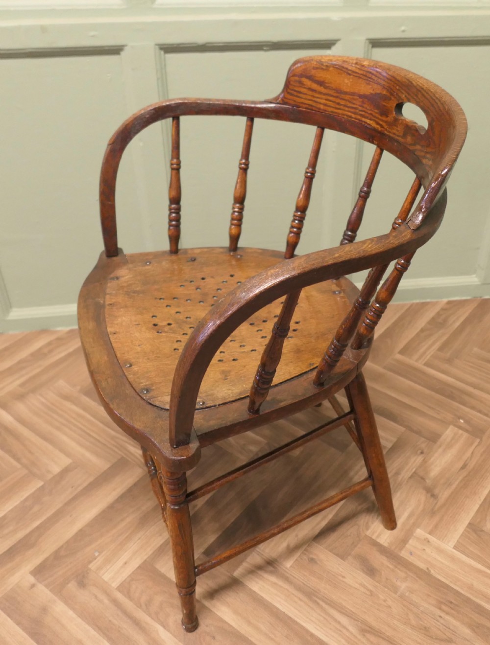 An antique oak smokers bow armchair featuring turned spindles, a curved top crest rail with a cut-out handle, and a perforated wooden seat panel. View II