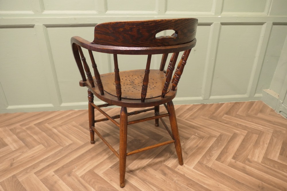 An antique oak smokers bow armchair featuring turned spindles, a curved top crest rail with a cut-out handle, and a perforated wooden seat panel. View III