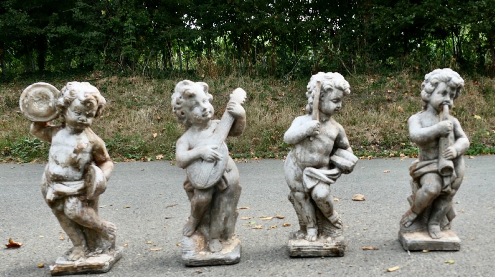 A set of four weathered grey cast stone cherub statues depicted playing musical instruments.