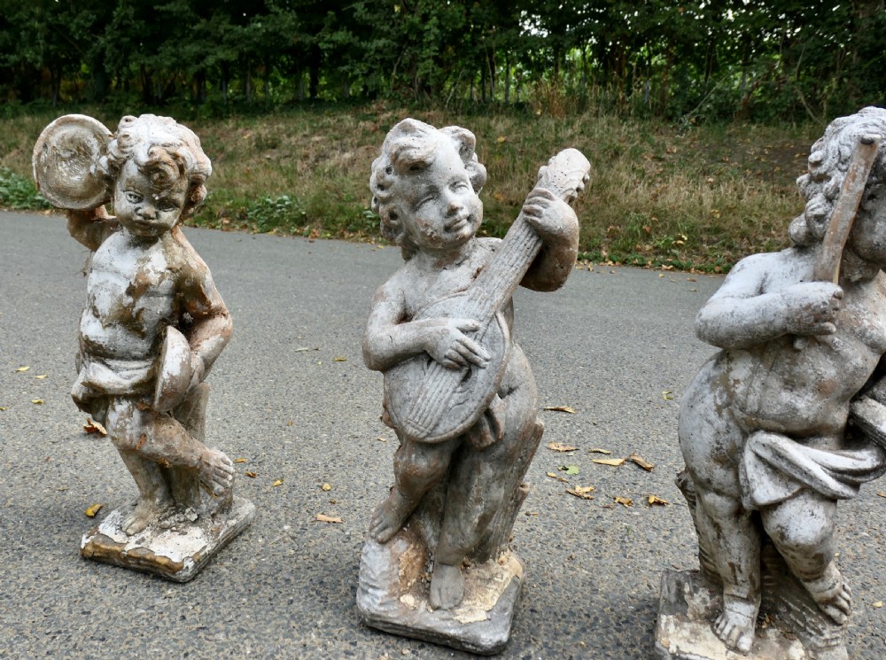 A set of four weathered grey cast stone cherub statues depicted playing musical instruments. View V