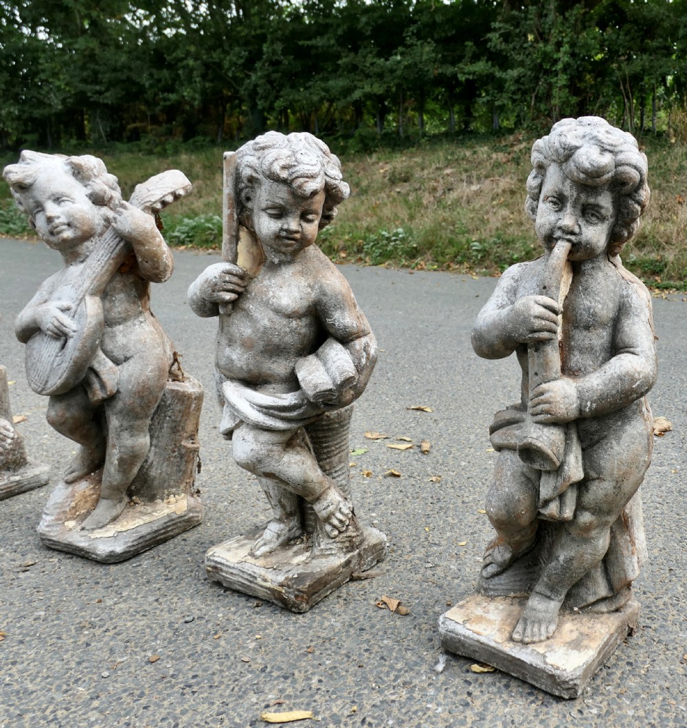 A set of four weathered grey cast stone cherub statues depicted playing musical instruments. View VI